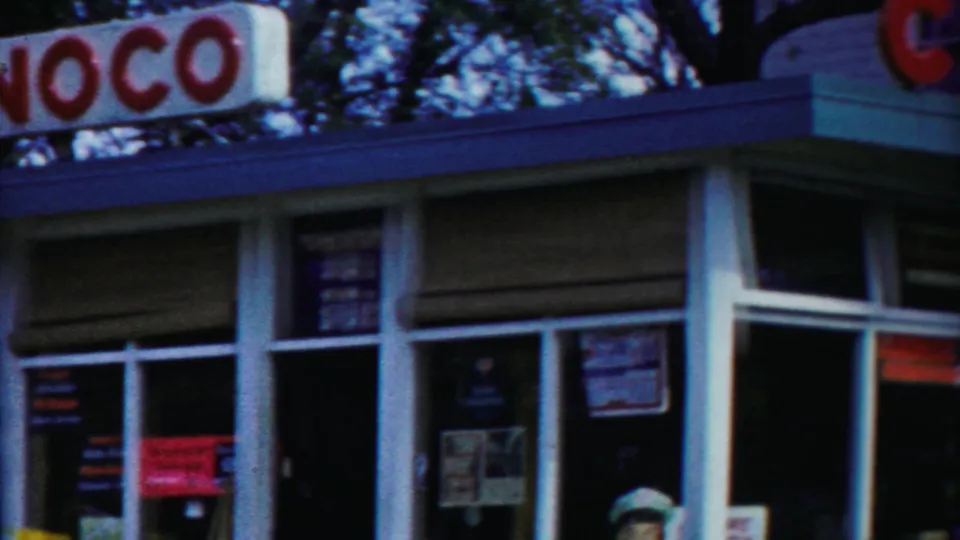 Conoco service-station frontage in Cheyenne County, Kansas, with red lettering, white-framed windows, and posted signs visible through soft 8mm focus.