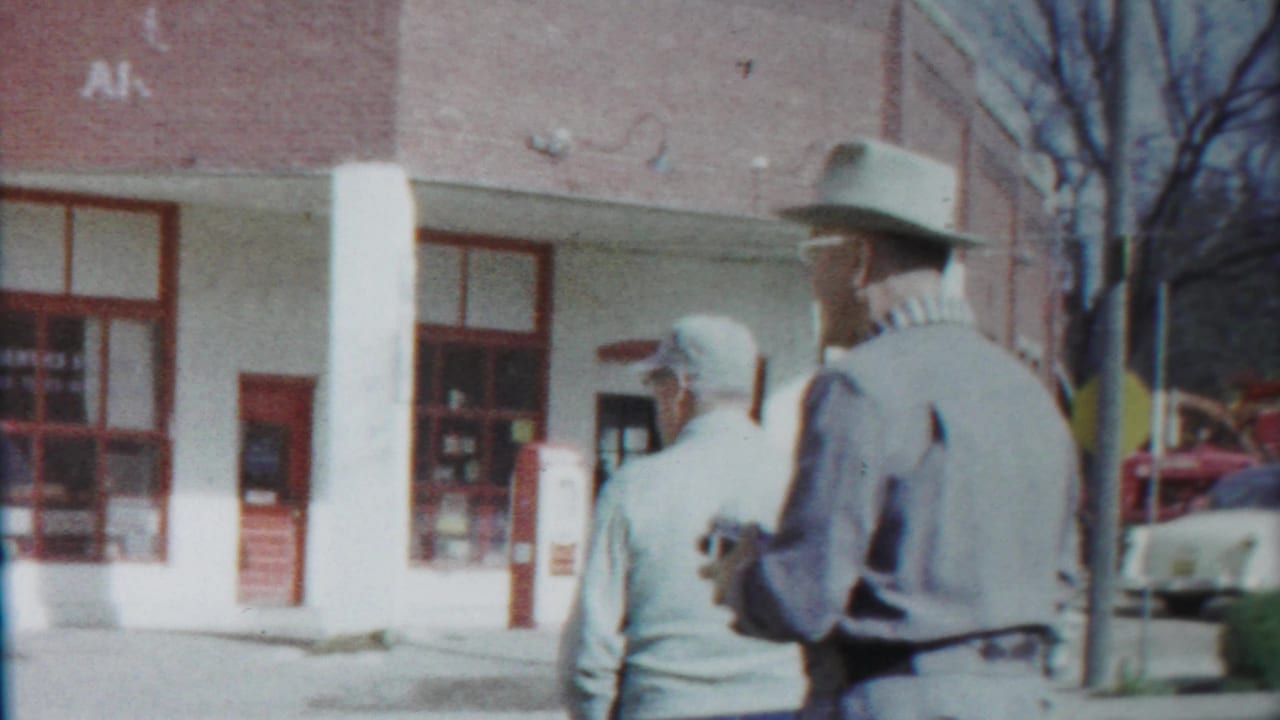 The closing frame shows the two men from behind on a 1958 Cheyenne County sidewalk, with a brick storefront and parked cars nearby.
