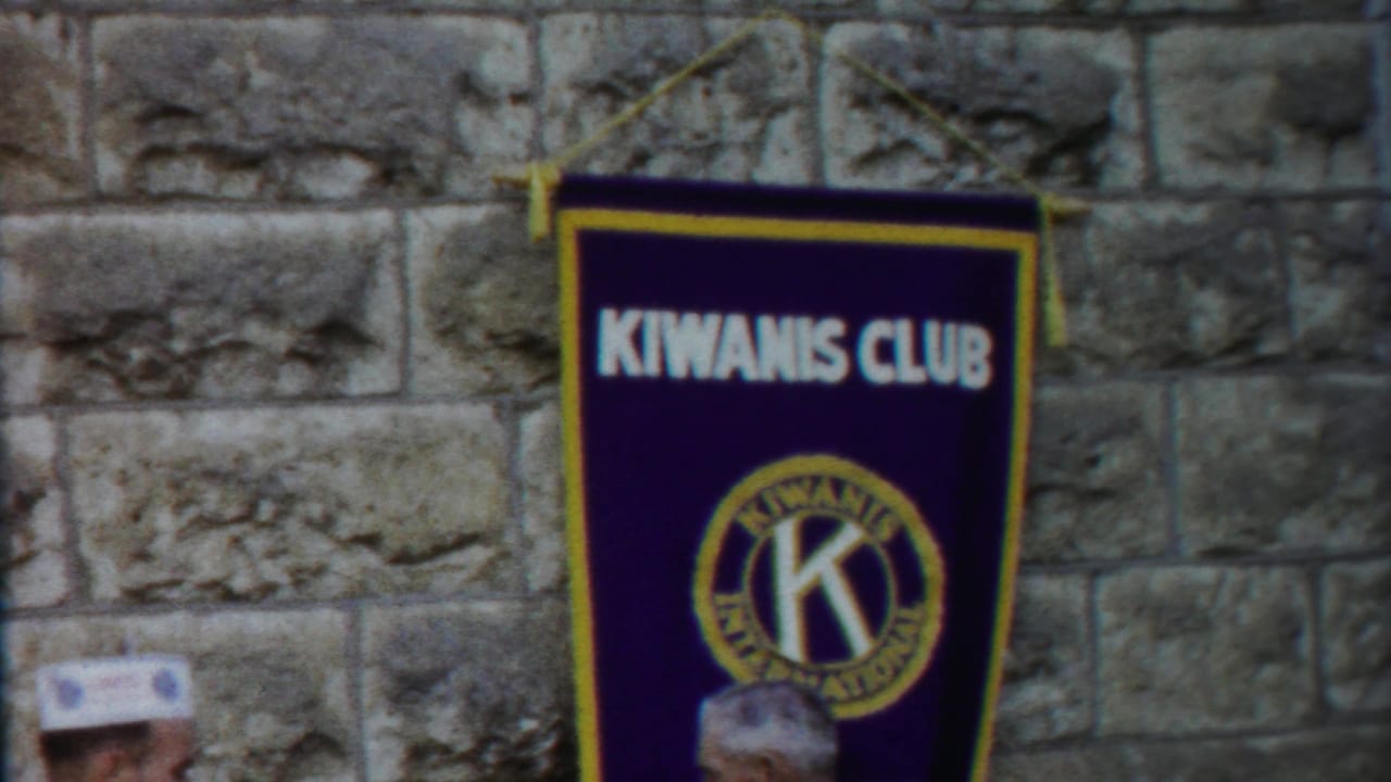A 1958 Kansas 8mm frame shows the Kiwanis Club banner against stonework, with only a partial attendee visible at the bottom.