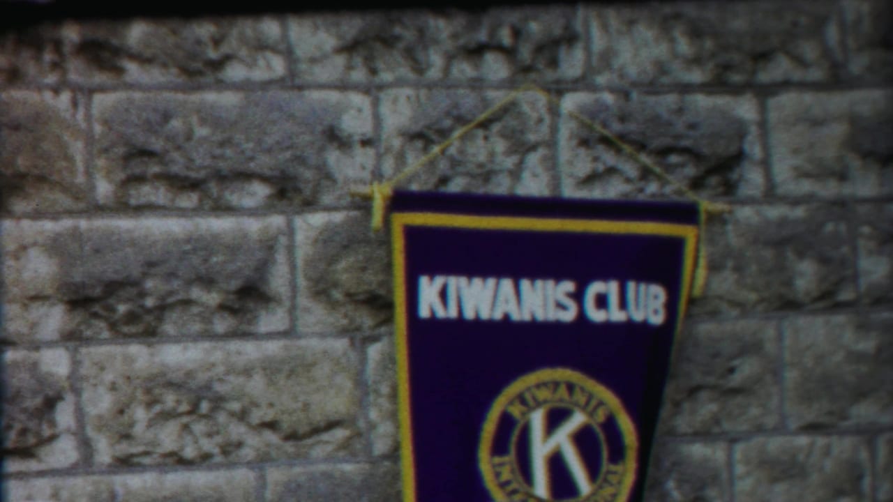 Final 1958 Kansas frame with the Kiwanis Club banner shifted to the right against a rough stone wall.