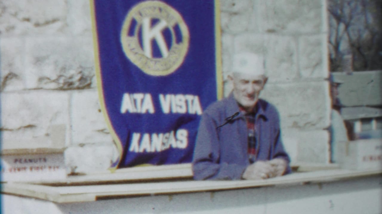 Smiling older man in a white hat stands near the Alta Vista Kansas Kiwanis banner during the 1958 parade clip.