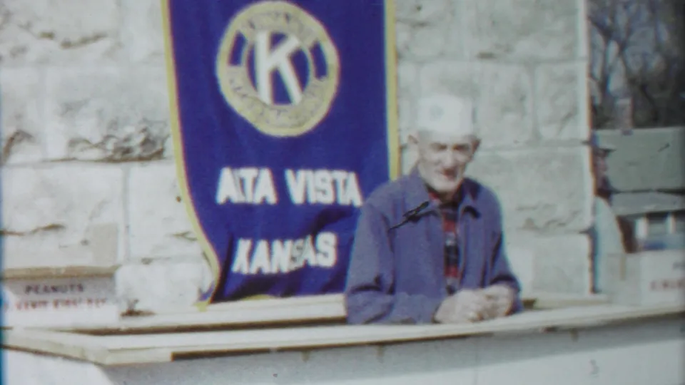 Smiling older man in a white hat stands near the Alta Vista Kansas Kiwanis banner during the 1958 parade clip.