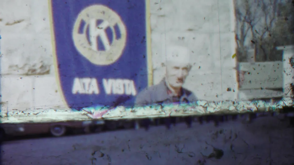 Alta Vista Kansas Kiwanis banner dominates the frame while the older man is partly visible beside the stone wall.