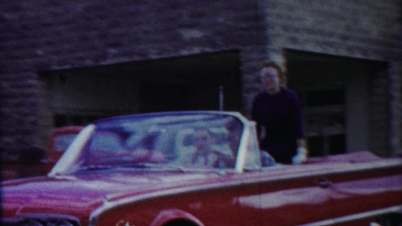 A woman in a dark top stands beside the red convertible in this 1958 Cheyenne County, Kansas home-movie frame.