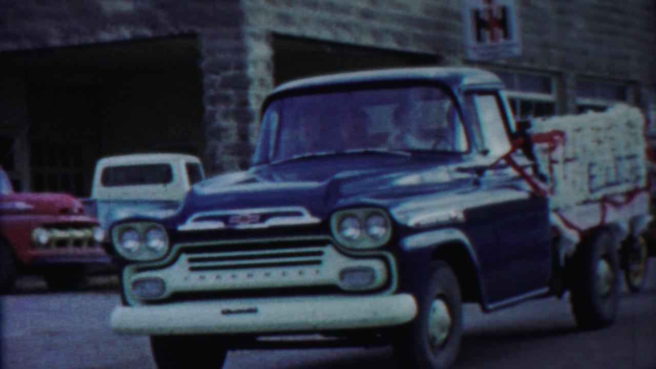 Blue Chevrolet pickup with white bumper in front of a stone building.