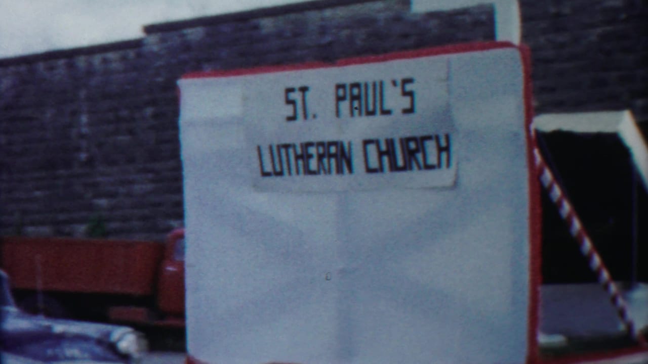 1958 Cheyenne County home-movie frame showing a St. Paul's Lutheran Church sign next to a red-trimmed parade float.