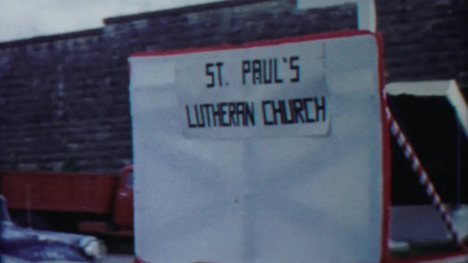 1958 Cheyenne County home-movie frame showing a St. Paul's Lutheran Church sign next to a red-trimmed parade float.