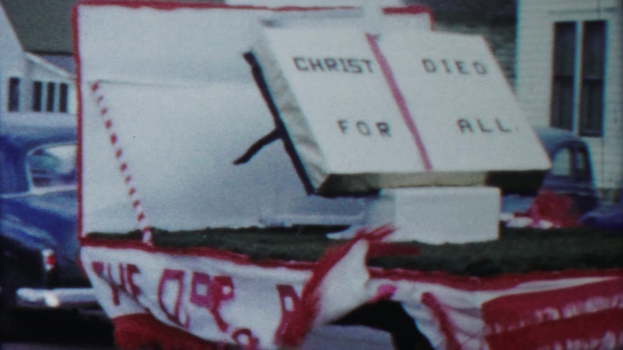 1958 Cheyenne County, Kansas parade float with an open-book religious sign and red-and-white trim passing parked cars.