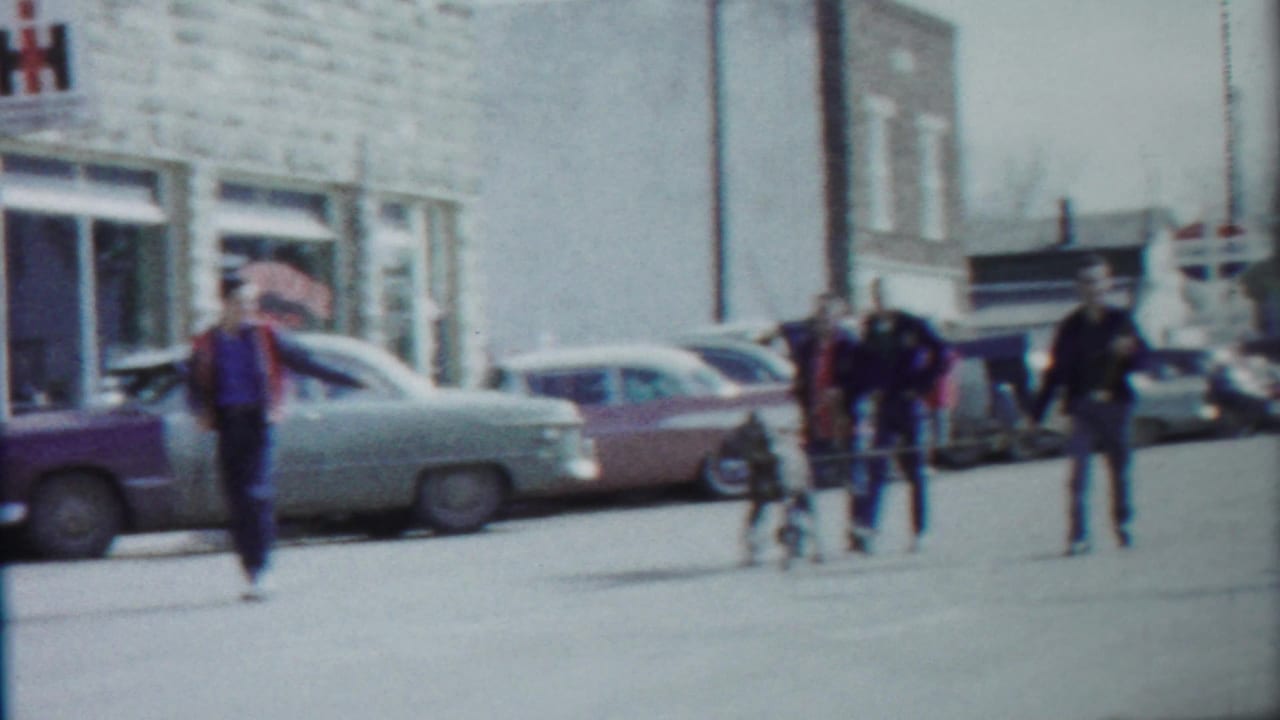 A street view in Cheyenne County, Kansas shows pedestrians near parked mid-century cars after the parade float passes from view.
