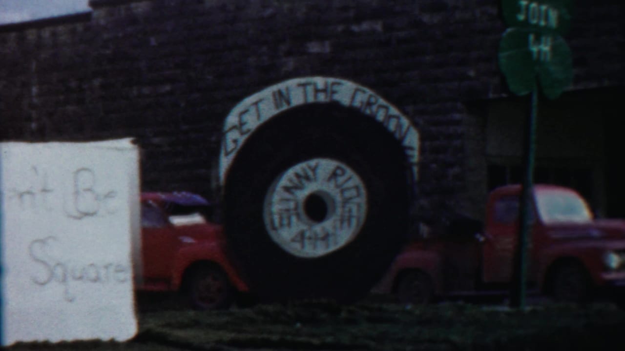 Large parade tire display with 4-H wording, handmade sign edge, and red vintage trucks on a 1958 Cheyenne County street.