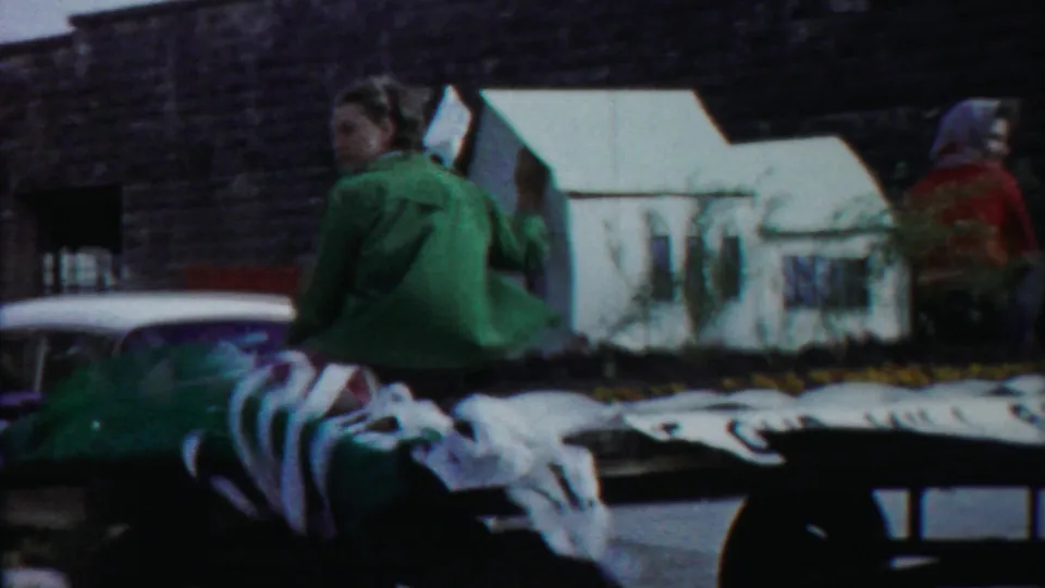 1958 Cheyenne County Kansas home-movie frame showing riders on a decorated float with a miniature white house and flowers.