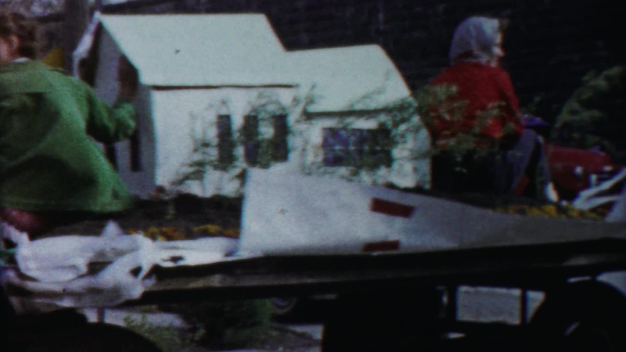 Float riders seated near a miniature white house and floral decorations on a parade platform.