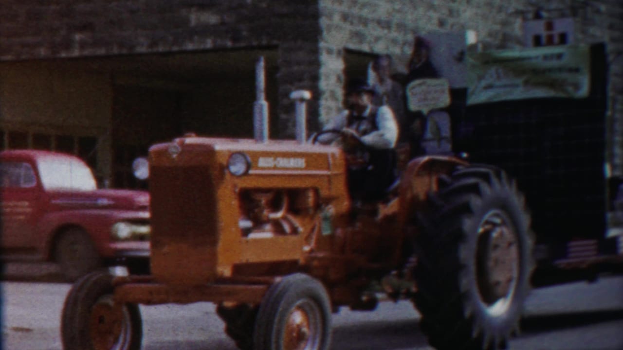 1958 Cheyenne County, Kansas parade view with an orange Allis-Chalmers tractor pulling a decorated float past a red pickup.