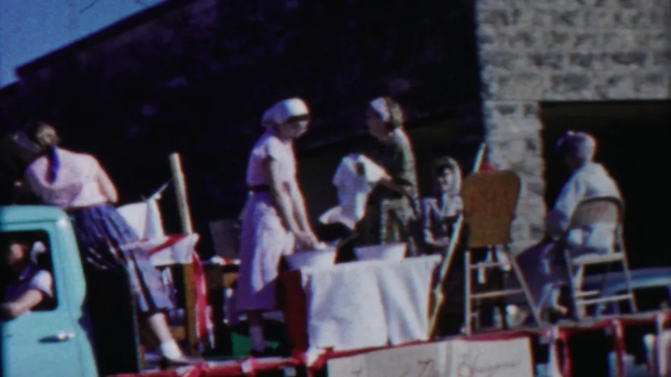 1958 Cheyenne County, Kansas parade float with women in aprons and headscarves around a table, with a truck cab at frame left.