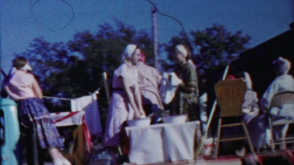 1958 Cheyenne County, Kansas parade float showing women in period dress around a table, with vintage cars and 4-H-themed props nearby.