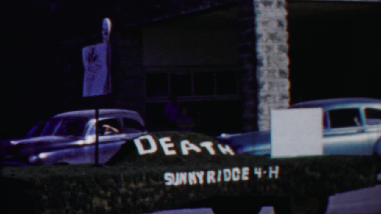1958 Cheyenne County, Kansas home-movie frame showing a dark sedan near a hedge sign reading DEATH SUNNYRIDGE 4-H.