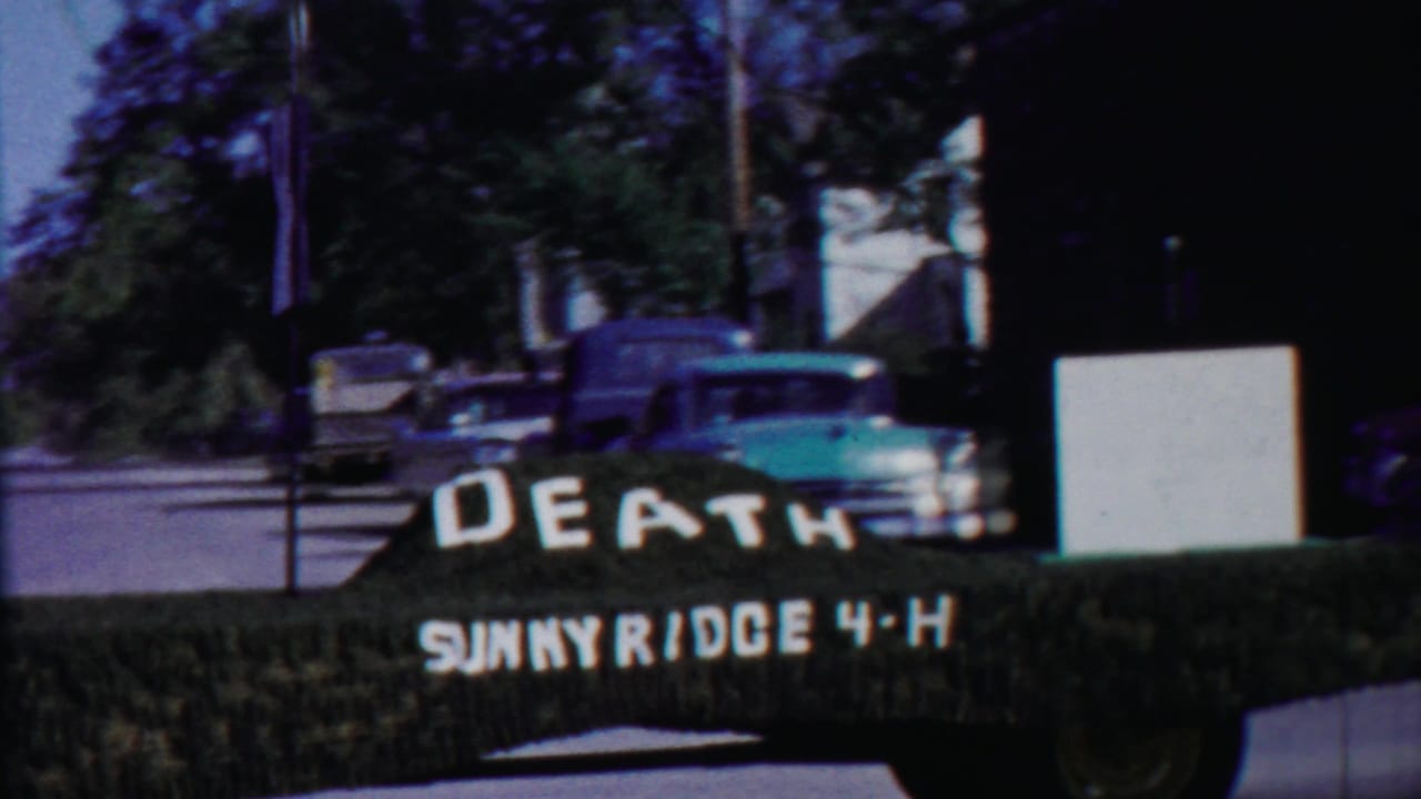 Roadside home-movie view in Cheyenne County, Kansas, with a pickup, street signs, trees, and the DEATH SUNNYRIDGE 4-H display.