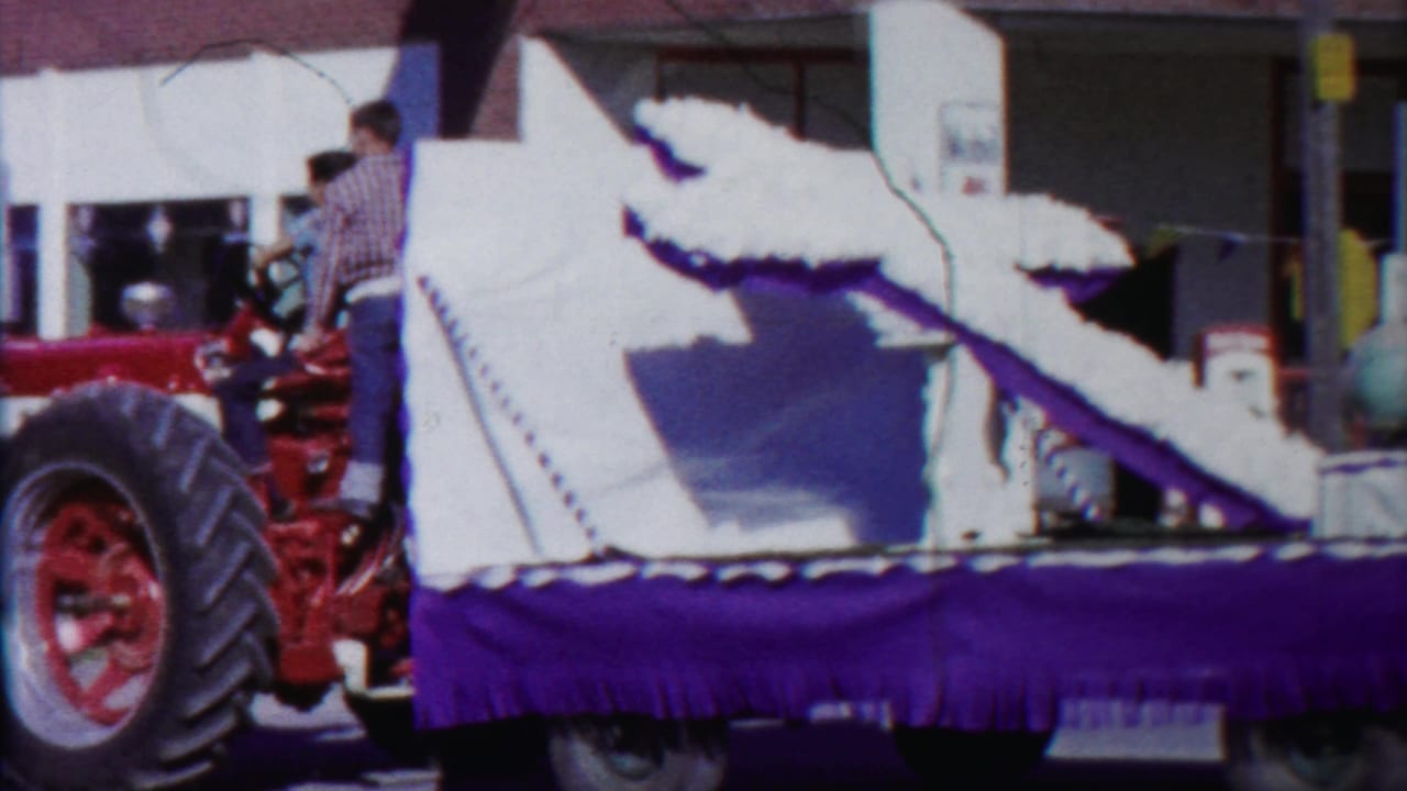 A red tractor pulls or stands beside a float with a large white horse figure during the 1958 Cheyenne County, Kansas home movie.
