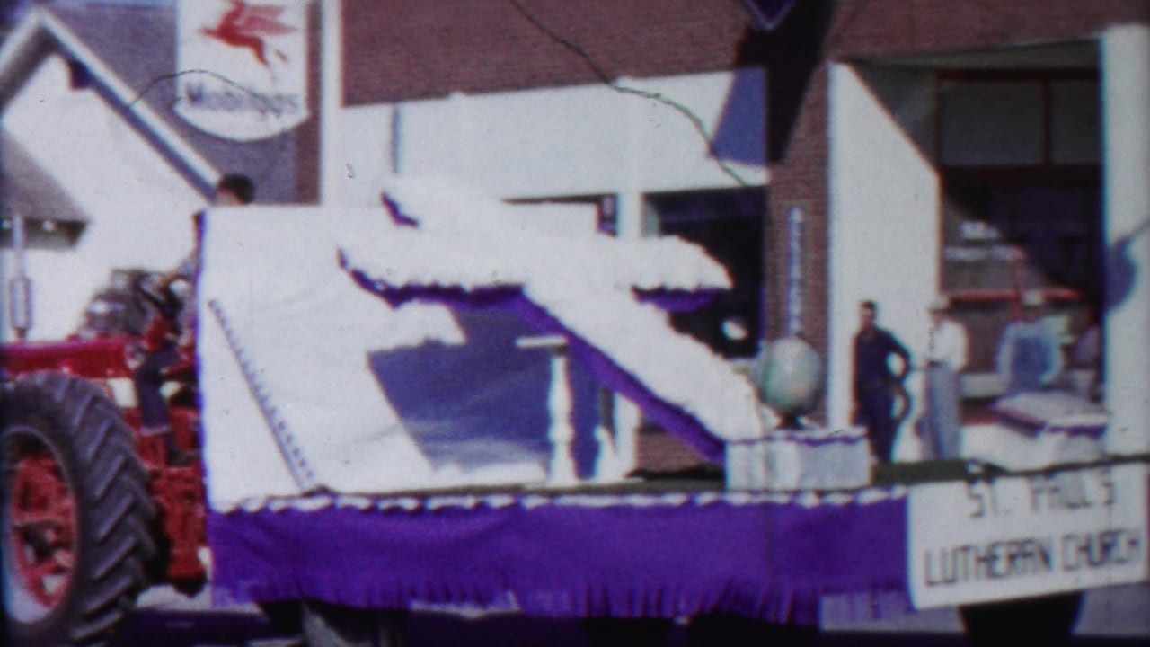 Church float with globe prop passing a service-station storefront and spectators.