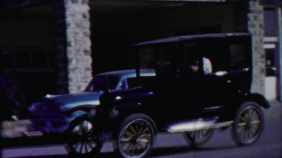 Dark early-style automobile seen on the parade route near a stone-fronted commercial building in the Cheyenne County, Kansas footage.