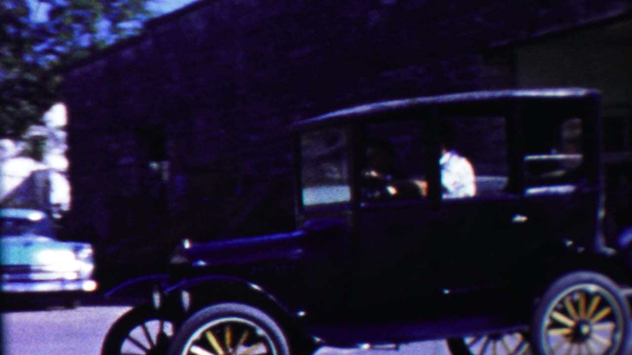 Black vintage car with driver passing in front of a dark building.
