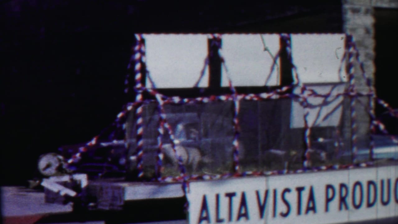 Parade float side view with pigs, ribbon trim, and partial Alta Vista Produce sign.