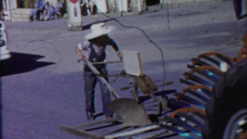 In documented 1958 Cheyenne County, Kansas footage, a man in overalls pulls a plow-like implement along a paved street.