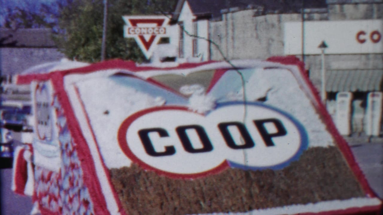 COOP parade float passing in front of a Conoco gas station sign.