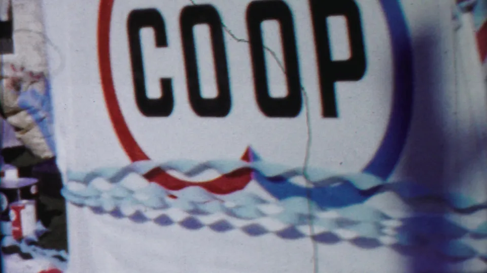 Tight 1958 home-movie view of the COOP float lettering with red, white, and blue decorative trim.