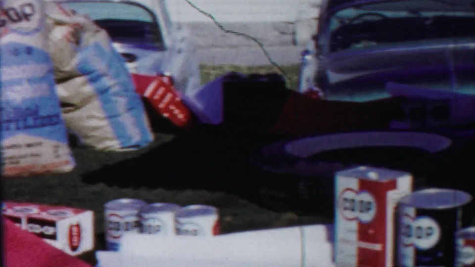 COOP boxed goods, cans, and sack products are grouped outdoors beside a classic car in the supplied 1958 Cheyenne County footage.