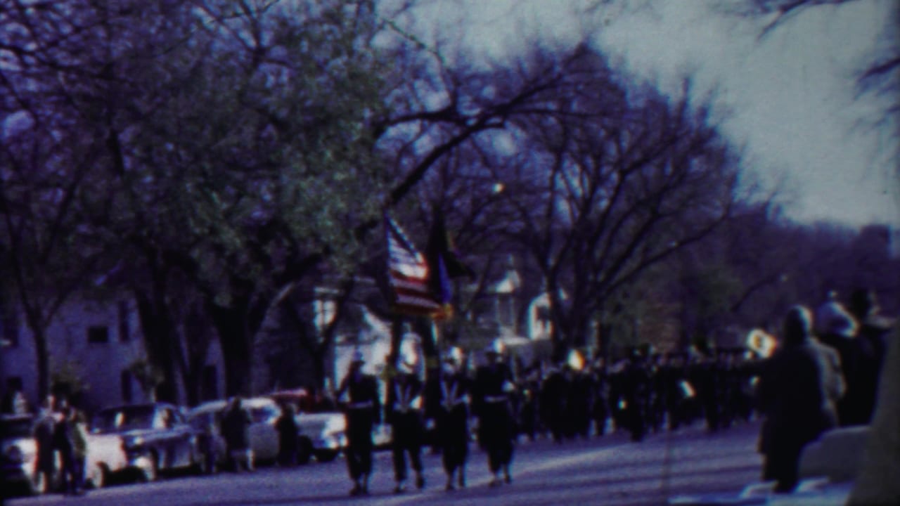 1958 Cheyenne County, Kansas parade view with a marching band, American flag, spectators, and 1950s cars along the curb.