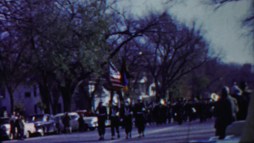 1958 Cheyenne County, Kansas parade view with a marching band, American flag, spectators, and 1950s cars along the curb.