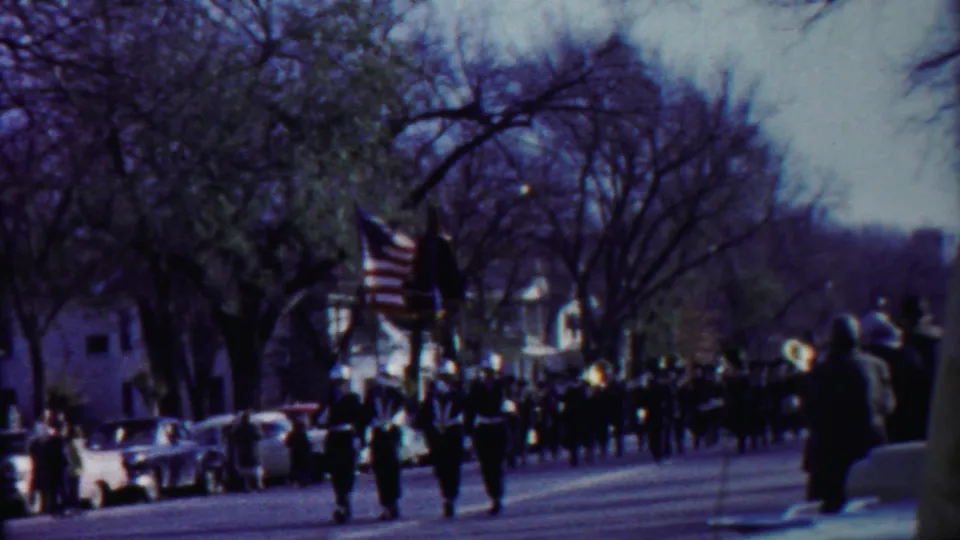Cheyenne County, Kansas parade frame showing uniformed marchers carrying an American flag and another banner on a broad street.