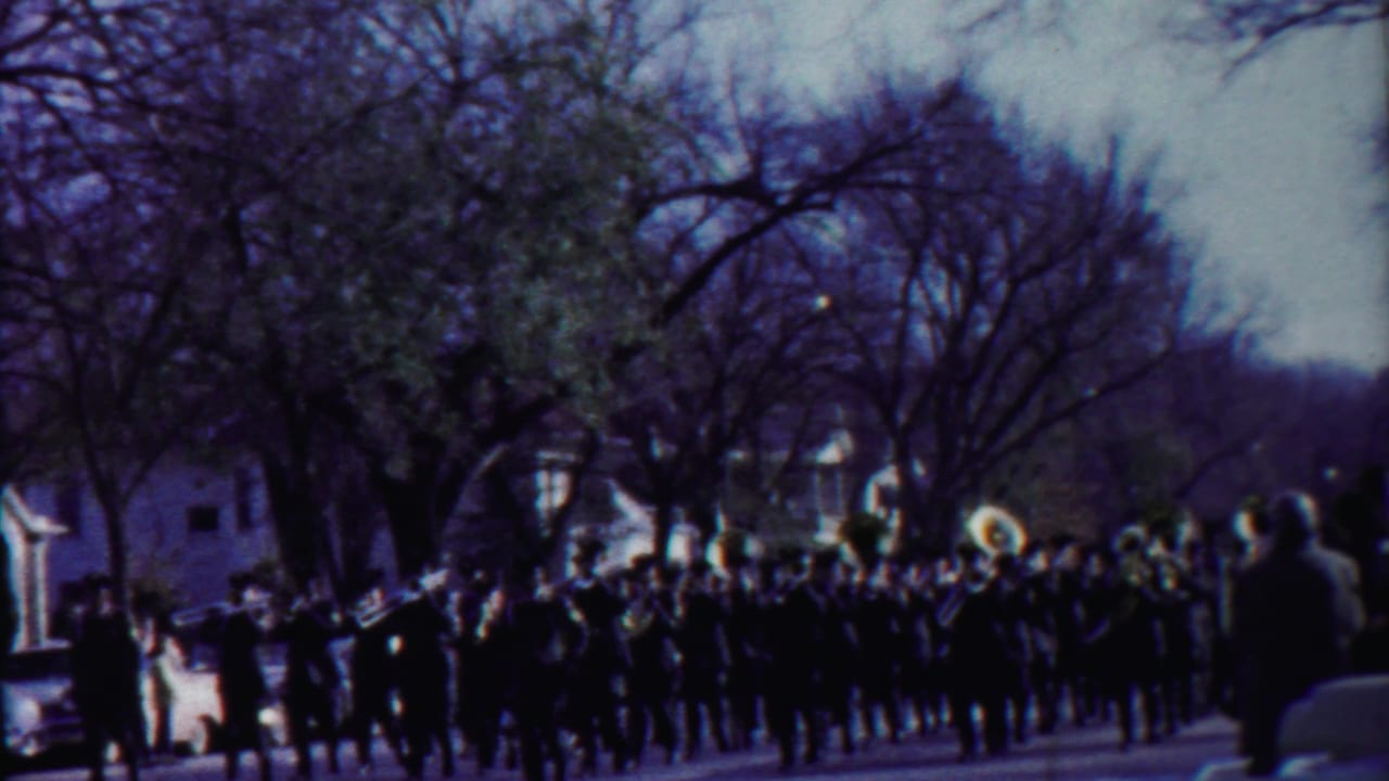 1958 8mm frame of a small-town Kansas band parade, seen from a roadside spectator position.