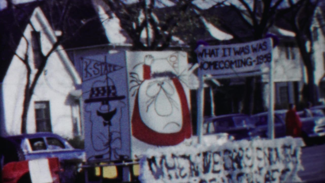 Decorated parade float in Cheyenne County, Kansas, with cartoon panels and a sign reading homecoming 1958 near parked cars.