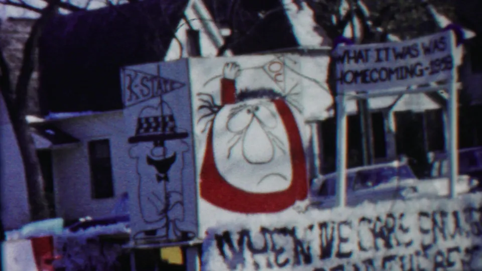 Close 8mm view of the Kansas homecoming parade float, showing hand-drawn character art and partially readable painted signage.