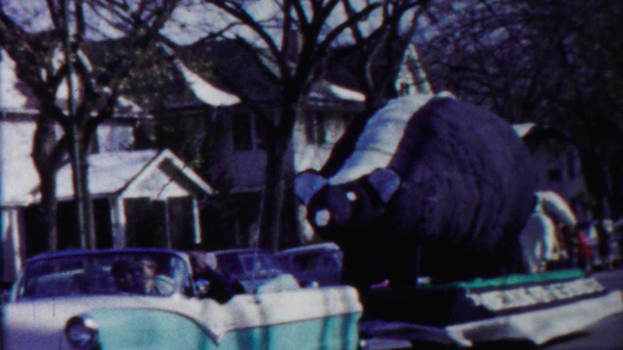 A large bear-shaped parade float moves through a Cheyenne County, Kansas residential street in 1958 home-movie footage.