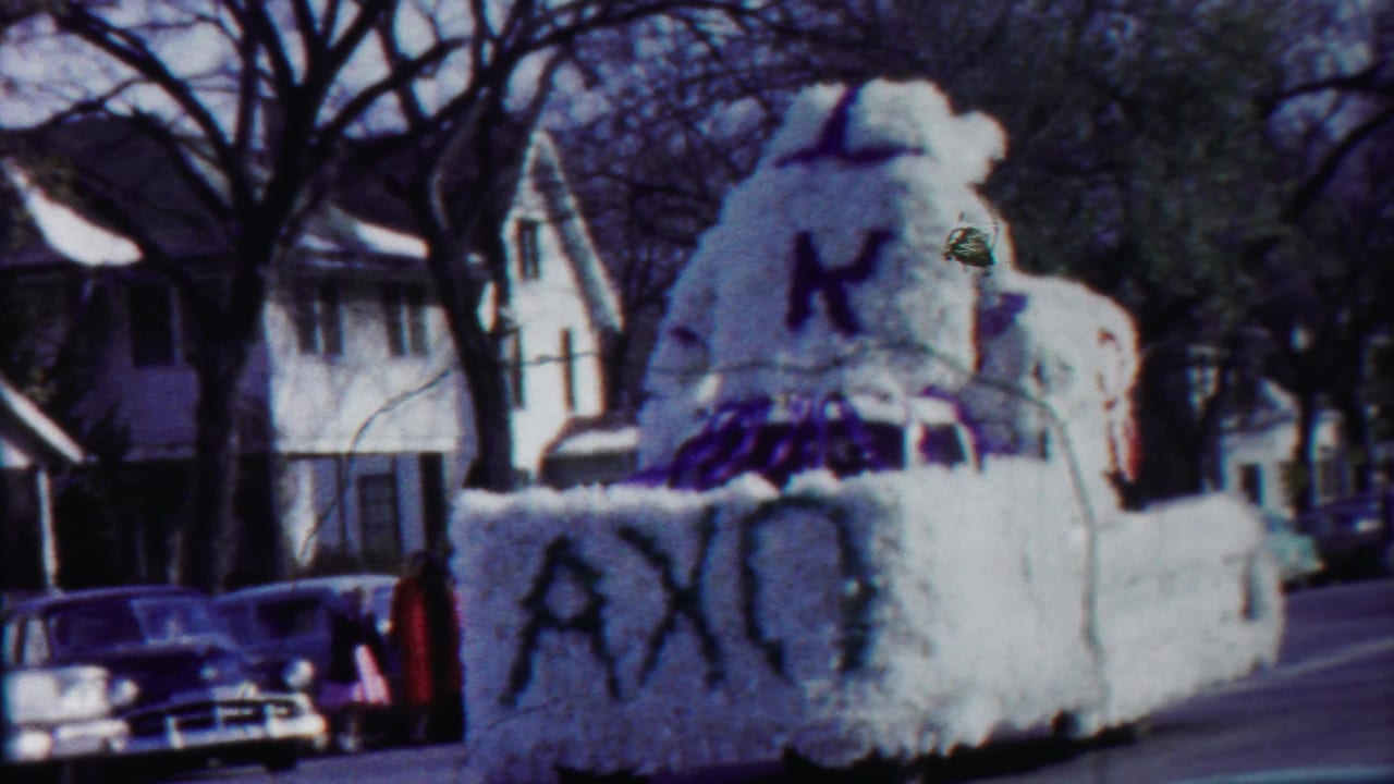 White flower-covered parade float passing parked cars on a residential street.