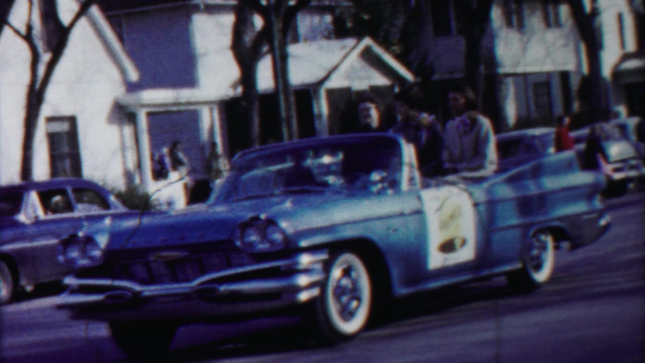 A light blue mid-century convertible with white-wall tires passes residential houses during the 1958 Cheyenne County, Kansas parade.
