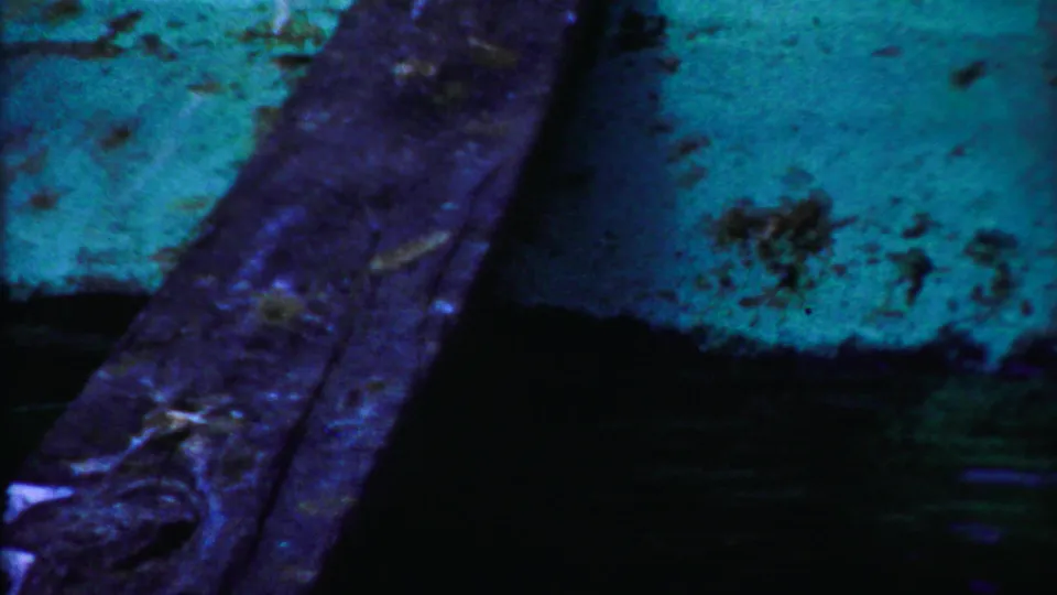1958 8mm frame from Cheyenne County, Kansas showing a close, shadowed view of weathered boards or stone with strong blue-green film color shift.