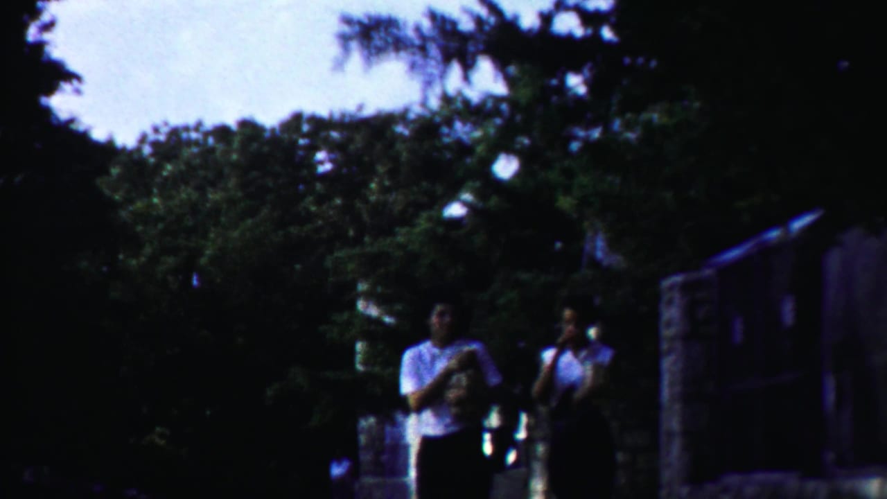 Two young women in white tops walk through a leafy outdoor setting in Cheyenne County, Kansas, 1958 home-movie footage.