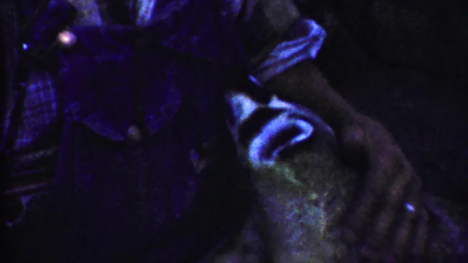Dim 1958 Kansas home-movie frame with the dog turned beside a person's dark clothing and arm, affected by strong purple color shift.