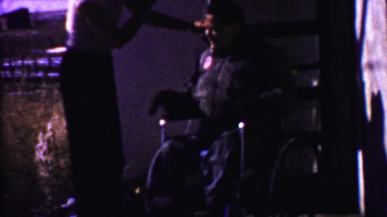 Standing man and seated man silhouetted in a dim interior near a doorway or window.