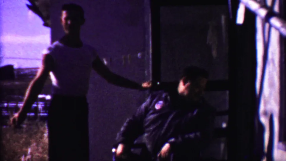 The 1958 Kansas 8mm frame shows the standing man at the doorway area while the seated man turns his face upward on the porch.