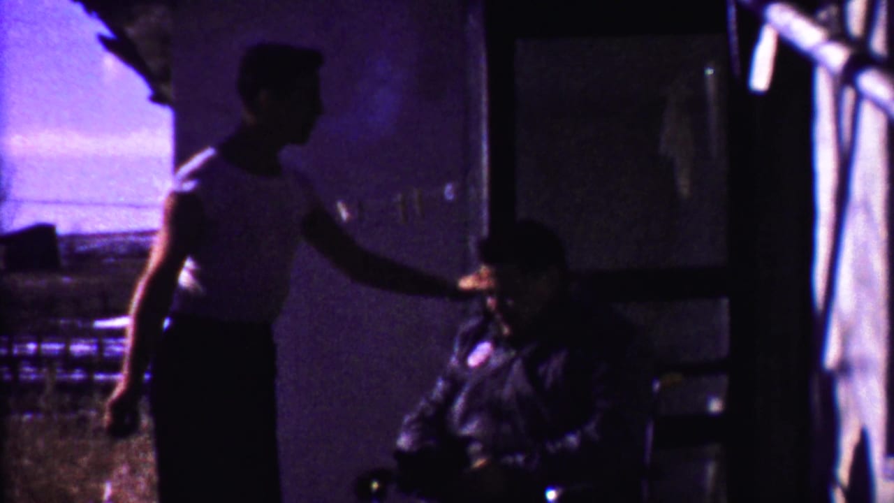 Standing man extends his hand toward a seated man in shadow near the wall.