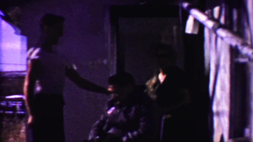 Near the end of the clip, the son remains beside his seated father while the doorway area is heavily shadowed.