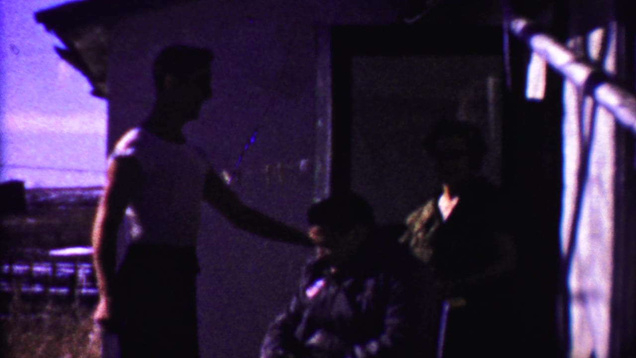 Standing youth beside a seated man with a woman in shadow near a doorway.