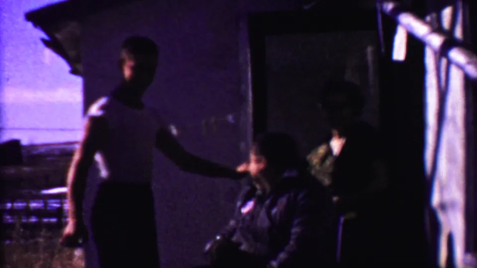 The youth appears to speak or gesture toward the seated man, with the doorway and woman partly obscured by deep shadow.