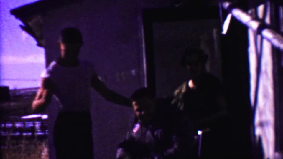 The final frame keeps the family group in shadow, with the youth at left, the seated man turned slightly, and the woman near the dark doorway.
