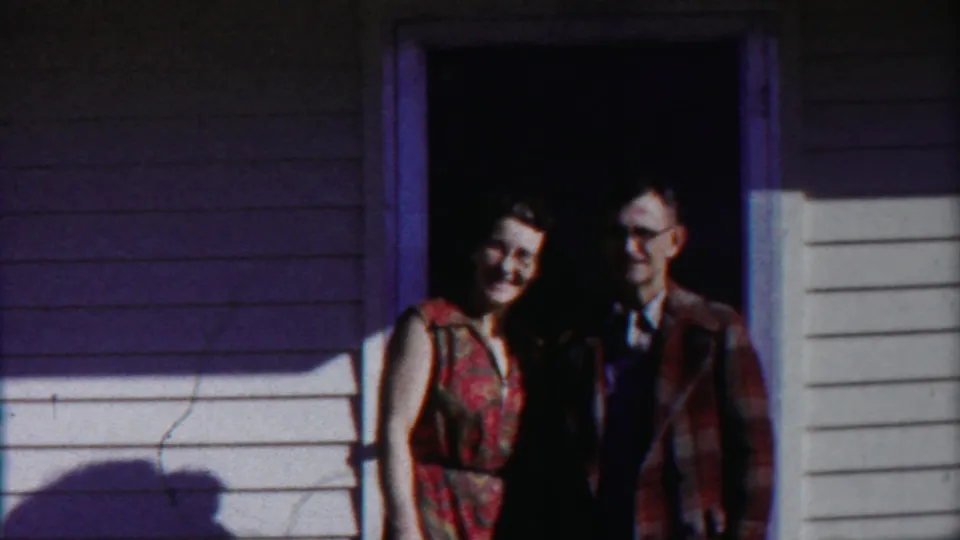 The couple remains in the doorway, faces partly shadowed against a dark interior and bright exterior siding.